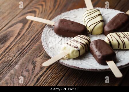 Des pop-sutes au chocolat au lait sur un bâtonnet. Des glaces à la crème glacée recouvertes de chocolat blanc et foncé sur l'assiette sur fond de bois. Espace pour le texte. Choc Banque D'Images