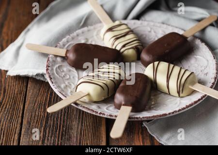 Des pop-sutes au chocolat au lait sur un bâtonnet. Des glaces à la crème glacée recouvertes de chocolat blanc et foncé sur l'assiette sur fond de bois. Espace pour le texte. Choc Banque D'Images