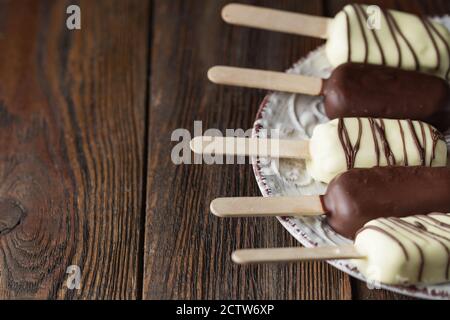 Des pop-sutes au chocolat au lait sur un bâtonnet. Des glaces à la crème glacée recouvertes de chocolat blanc et foncé sur l'assiette sur fond de bois. Espace pour le texte. Choc Banque D'Images