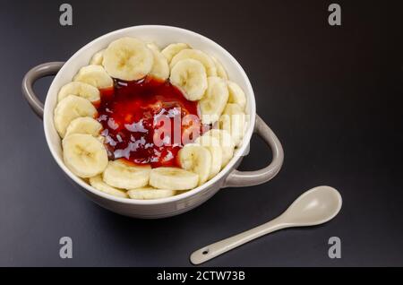 Flocons d'avoine avec bananes, dans un bol gris-blanc avec une cuillère blanche sur fond noir gros plan. Petit déjeuner sain. Banque D'Images