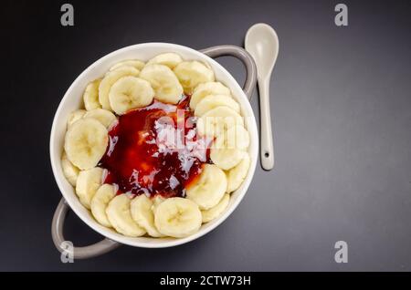 Flocons d'avoine aux bananes, confiture dans un bol gris-blanc avec une cuillère blanche sur fond noir, vue de dessus, espace de copie. Petit déjeuner sain. Banque D'Images