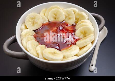 Flocons d'avoine avec bananes, dans un bol gris-blanc avec une cuillère blanche sur fond noir gros plan. Petit déjeuner sain. Banque D'Images