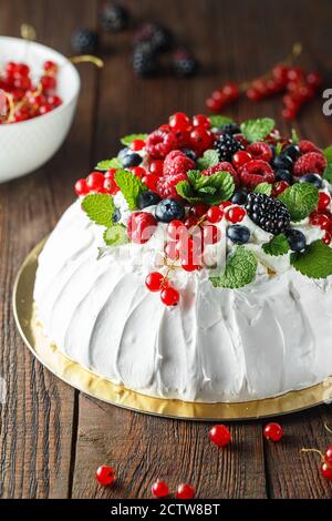 Gâteau Pavlova à la crème et aux baies fraîches sur fond de bois. Gros plan sur le dessert Pavlova avec des fruits de la forêt et de la menthe. Photographie alimentaire Banque D'Images