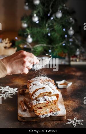 Stollen est un pain aux fruits à coque, aux épices, aux fruits secs ou confits, enrobé de sucre en poudre. Fermez les mains du chef avec le tamis métallique arrosé de la cak Banque D'Images