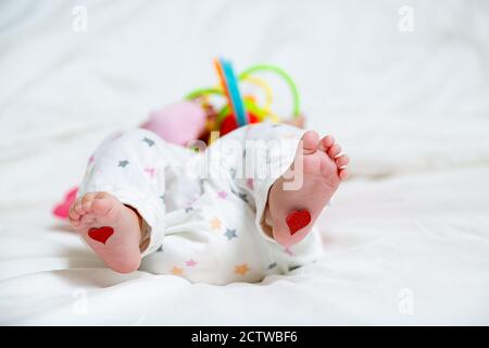 Bébé repose avec les coeurs sur leurs pieds. Un nouveau-né est allongé sur le lit et joue des jouets Banque D'Images