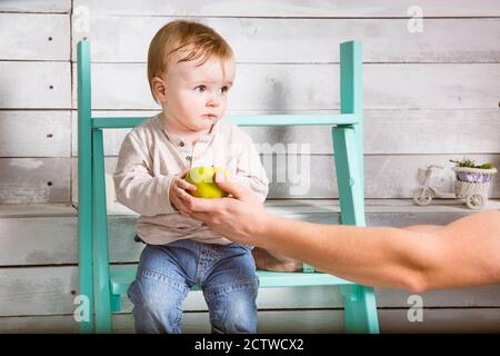 Un petit garçon triste prend une pomme de son père. Il est assis sur les marches à l'intérieur. Fond en bois blanc Banque D'Images