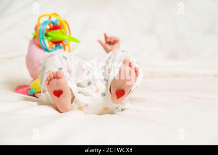 Bébé repose avec les coeurs sur leurs pieds. Un nouveau-né est allongé sur le lit et joue des jouets Banque D'Images