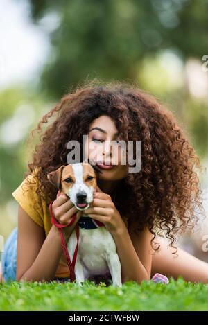 brunette, une femme maurique qui fait des lèvres tout en se détendant avec un chien terrier jack russell sur de l'herbe verte Banque D'Images