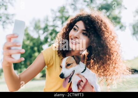 jeune femme maussée qui câlin jack russell chien terrier tout en emportant le selfie sur le téléphone portable dans le parc Banque D'Images