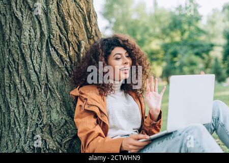 Objectif sélectif de la femme en imperméable ayant un appel vidéo ordinateur portable dans le parc Banque D'Images