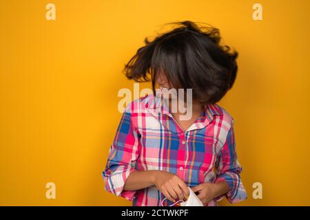 Jeune femme agitant ses cheveux sur fond jaune en studio. Brunette brandit ses cheveux et tient un masque médical dans sa main. Photo de haute qualité Banque D'Images