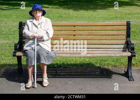 Femme de quatre-vingt-dix ans avec un bâton de marche assis sur le banc du parc. ROYAUME-UNI Banque D'Images