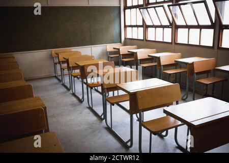 Vue latérale d'une salle de classe vide, avec des bureaux en formation et un tableau noir derrière eux, avec des fenêtres ouvertes par temps ensoleillé Banque D'Images