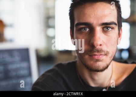 Portrait d'un homme caucasien portant des vêtements décontractés, assis près d'une table dans un café, regardant directement dans un appareil photo Banque D'Images