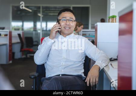 Élégant décontracté asiatique homme créatif d'affaires portant des lunettes assis à un bureau souriant, parlant sur un smartphone. Professionnel de la création avec Banque D'Images