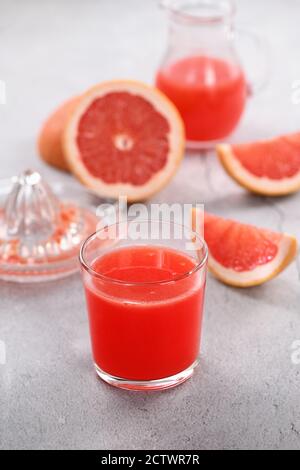 Un verre de jus de pamplemousse fraîchement préparé et des tranches de fruits frais sur un fond en béton léger. Boisson saine et alimentation. Gros plan Banque D'Images