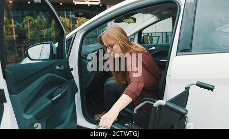 Jeune femme handicapée sortant de la voiture en fauteuil roulant. Photo de haute qualité Banque D'Images