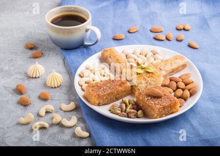 bonbons traditionnels arabes (basbus, kunafa, baklava), une tasse de café et de noix sur fond de béton gris et de textile bleu. vue latérale, gros plan. Banque D'Images