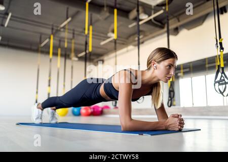 Pleine longueur de jeune belle femme en vêtements de sport faisant de la planche et de travailler ses muscles de noyau à la salle de gym. Banque D'Images