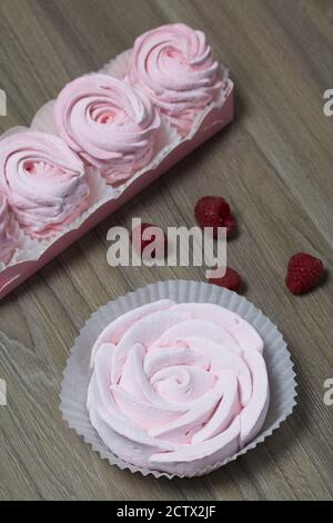 Guimauve rose dans une boîte cadeau. À proximité se trouve un bouquet de plusieurs framboises. Banque D'Images