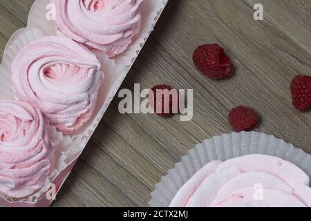 Guimauve rose dans une boîte cadeau. À proximité se trouve un bouquet de plusieurs framboises. Banque D'Images