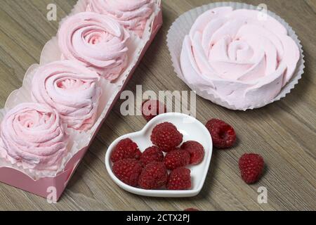 Guimauve rose dans une boîte cadeau. Un bouquet de framboises se trouve à proximité. Banque D'Images