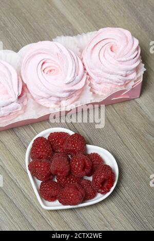 Guimauve rose dans une boîte cadeau. Un bouquet de framboises se trouve à proximité. Banque D'Images