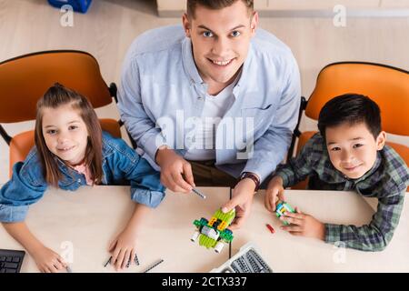 Vue de dessus des enseignants et des élèves multiethniques regardant la caméra tout en modélisant le robot dans la salle de classe Banque D'Images