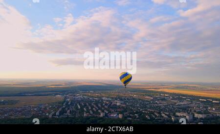 Vue aérienne par drone d'une montgolfière colorée survolant un parc vert dans une petite ville européenne au coucher du soleil d'été, région de Kiev, Ukraine Banque D'Images