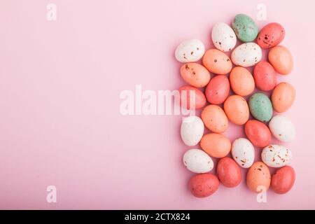 Bonbons colorés aux œufs de chocolat multicolores sur fond rose pastel. Dragées caramel, espace pour les copies, vue du dessus, ponte à plat. Banque D'Images