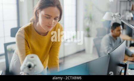 Jeune femme belle et créative assise à son bureau à l'aide d'un ordinateur portable. En arrière-plan Bright Office où diverse équipe de jeunes Banque D'Images