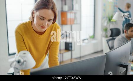 Jeune femme belle et créative assise à son bureau à l'aide d'un ordinateur portable. En arrière-plan Bright Office où diverse équipe de jeunes Banque D'Images