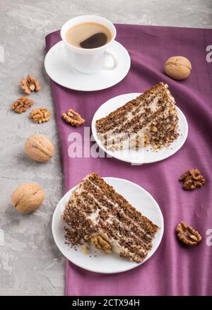 Gâteau fait maison avec crème au lait et noix, tasse de café sur fond de béton gris et textile violet. Vue latérale, gros plan. Banque D'Images