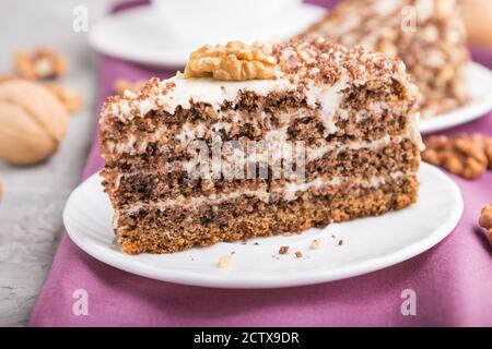 Gâteau maison avec crème au lait et noix, tasse de café sur fond de béton gris et textile violet. Vue latérale, gros plan, mise au point sélective. Banque D'Images