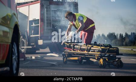 Sur la scène d'accident de la circulation automobile : brancards de pré-appariement paramédiques pour effectuer les premiers soins. Tirer le moteur en arrière-plan. Banque D'Images