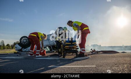 Sur la scène des accidents de la route : l'équipe de paramédicaux et de pompiers secourent les personnes blessées coincées dans un véhicule en retournement. Professionnels Banque D'Images