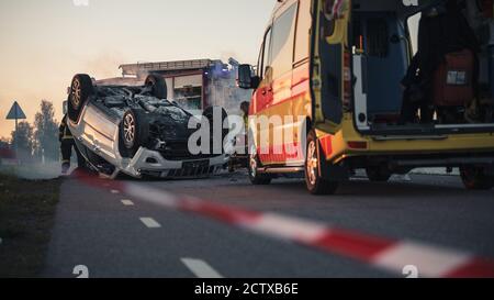 Sur la scène d'accident de la route en cas de retournement d'un véhicule qui se trouve sur son toit au milieu de la route après collision. Dans les Medics de fond Banque D'Images