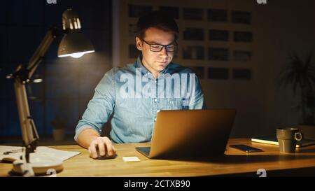 Homme professionnel assis à son bureau dans Office Studio travaillant sur un ordinateur portable dans la soirée. Homme analysant les statistiques. Banque D'Images