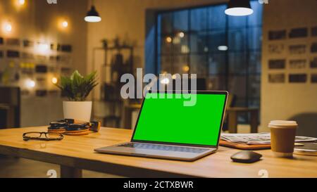 Maquette d'écran vert Stanting sur le bureau. En arrière-plan élégant studio moderne de bureau dans la soirée avec grande fenêtre CityScape Banque D'Images