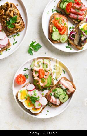 Sandwichs ouverts avec viande, légumes et fruits de mer sur plaque sur fond de pierre légère. Vue de dessus, plan d'appartement. Banque D'Images