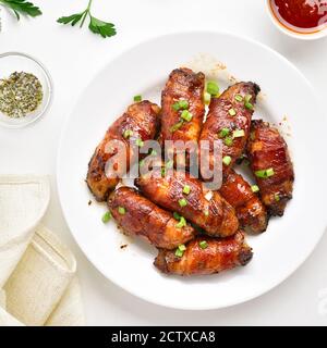 Ailes de poulet grillées enveloppées de bacon sur une assiette sur fond de pierre blanche. Vue de dessus, plan d'appartement Banque D'Images