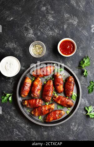 Ailes de poulet grillées enveloppées de bacon sur une assiette sur fond de pierre sombre. Vue de dessus, plan d'appartement Banque D'Images