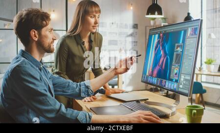 La directrice artistique féminine consulte un collègue concepteur, elle travaille sur un portrait dans le logiciel d'édition de photos. Ils travaillent dans un loft Cool Office. Ils ont l'air très Banque D'Images