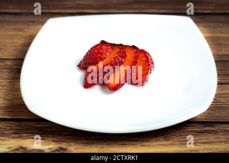 Vue aérienne d'une fraise coupée en tranches sur blanc plaque et fond en bois Banque D'Images