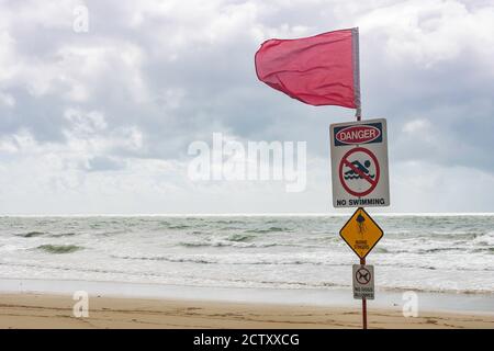 Queensland, Australie - 18 mars 2020 : panneaux d'avertissement et drapeau rouge sur une plage de Queensland, Australie, par jour nuageux. Banque D'Images