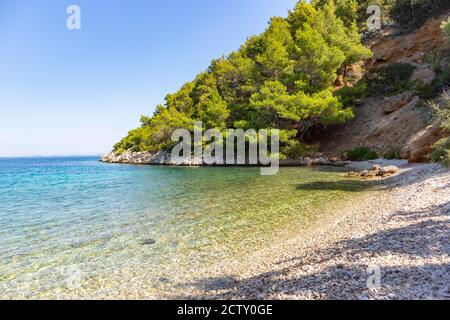 Collines escarpées couvertes de forêt dense de pins entourant la magnifique plage de galets blancs de Stiniva sur l'île de Hvar, destination touristique étonnante Banque D'Images