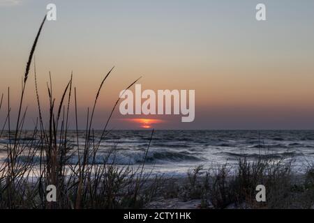 Coucher de soleil bas sur l'horizon caché dans le nuage avec orageux vagues de la mer et de l'herbe sauvage à l'avant Banque D'Images