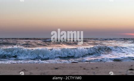 Vagues blanches et orageux sur la plage de sable de la côte de mer en gros plan avec ciel de coucher de soleil dans des couleurs pastel Banque D'Images