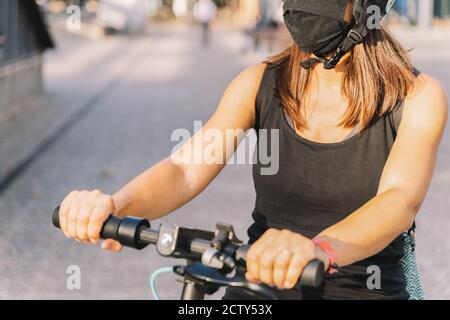 gros plan d'une jeune femme portant un masque de protection contre coronavirus dans un scooter électrique utilisant avec un arrière-plan flou dedans une ville Banque D'Images