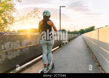 Jeune belle femme à bord d'un scooter électrique dans une ville parc - concept de mobilité personnelle durable Banque D'Images